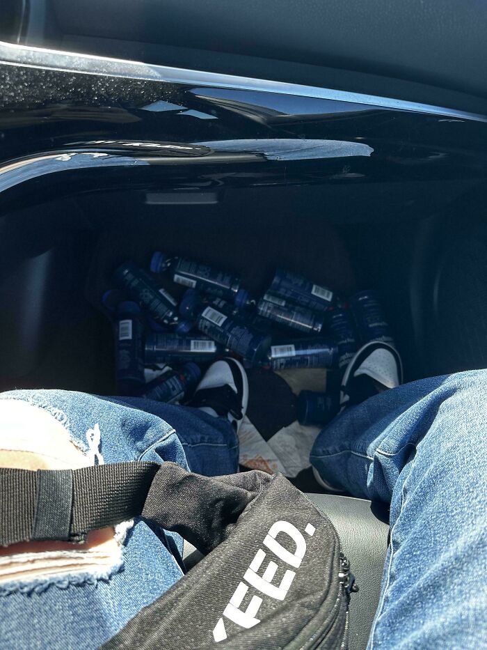 A person in ripped jeans sitting in a car with empty bottles scattered, highlighting weaponized incompetence.
