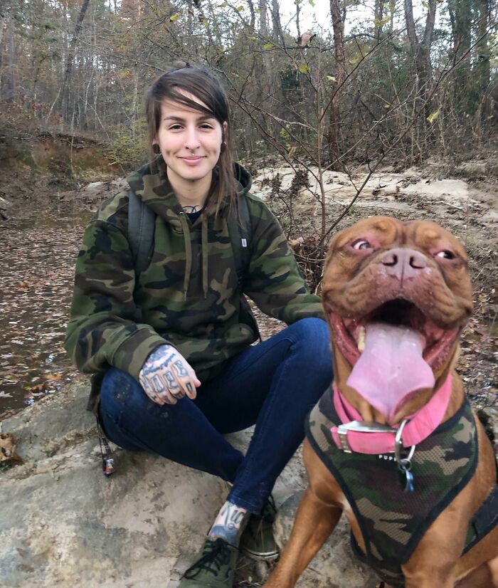 Person in camo hoodie sitting outdoors with happy dog in matching vest, embodying Thanksgiving right spirit.