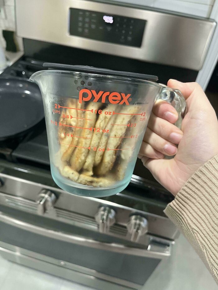 A person holding a Pyrex measuring cup filled with cooked sausages, exemplifying weaponized incompetence in cooking.