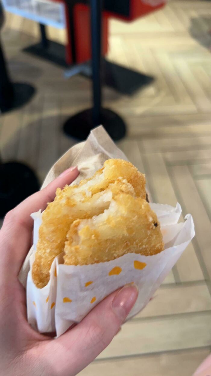 Person holding hash browns in paper wrapping at a fast-food restaurant.