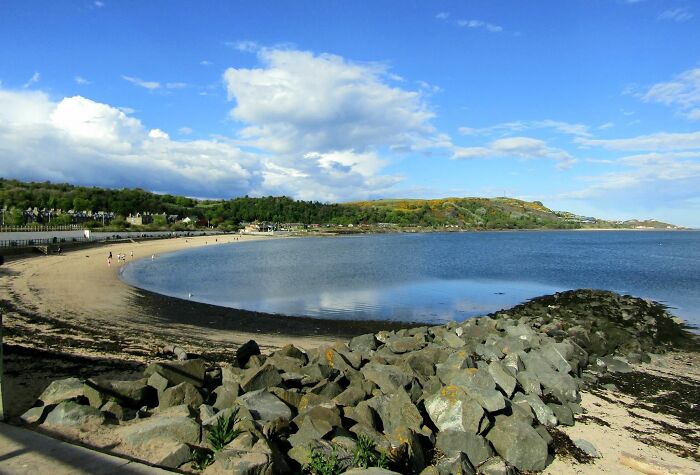 Scenic beach with rocky shoreline and calm water under a blue sky, showcasing interesting unedited natural beauty.