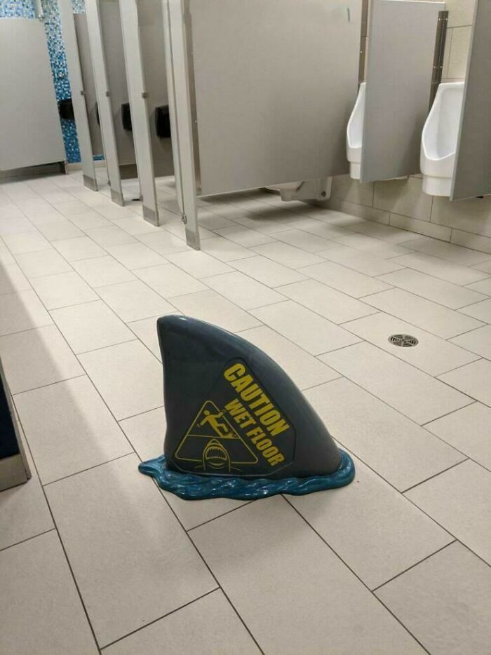Creative wet floor sign shaped like a shark fin in a restroom, showcasing designer ingenuity and innovation.