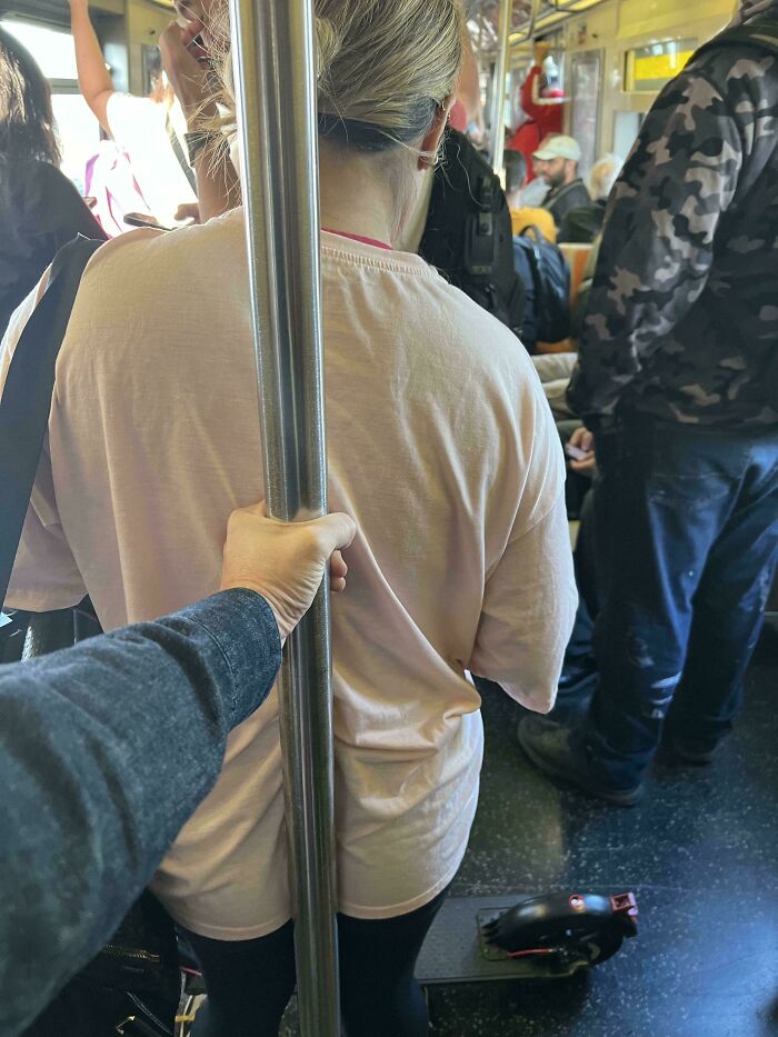Crowded subway with public transport passengers standing, one person holding a pole, creating an infuriating experience.
