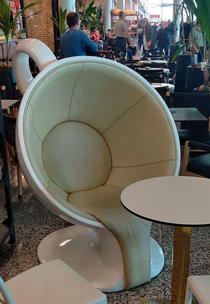 Creative designer chair resembling a coffee cup in a busy cafe setting.