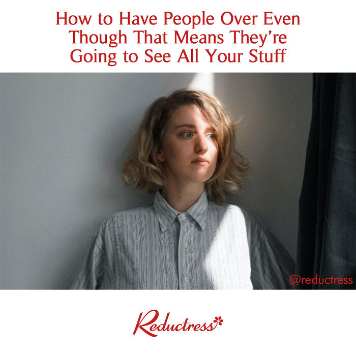 A woman in a light shirt stands by a window, expressing the humorous truth about hosting guests.