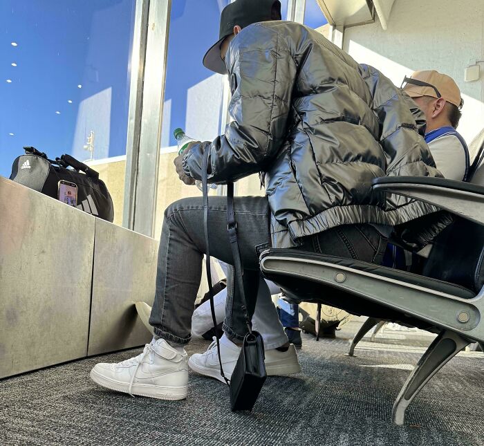 Traveler at airport gate in a puffer jacket, with legs on the seat, highlighting annoying plane passengers behavior.