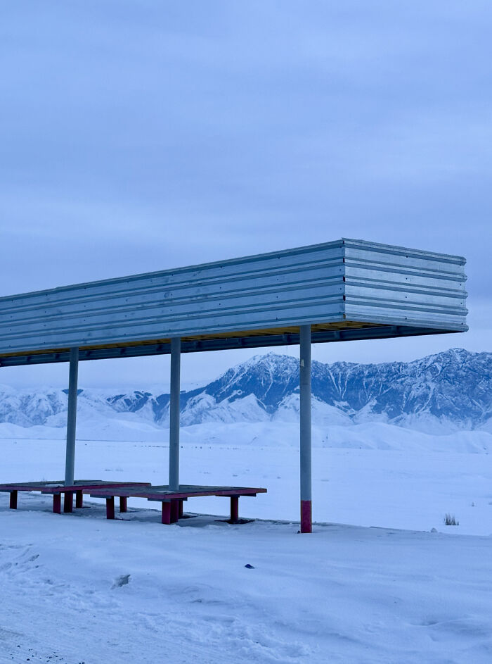 Metal shelter in snow-covered landscape with mountains in the background, illustrating ice-cold winter scenery.