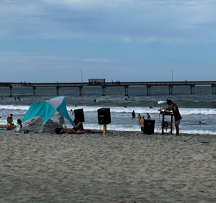 Beachgoer setting up large speakers near others relaxing by the shore, showcasing inconsiderate behavior.