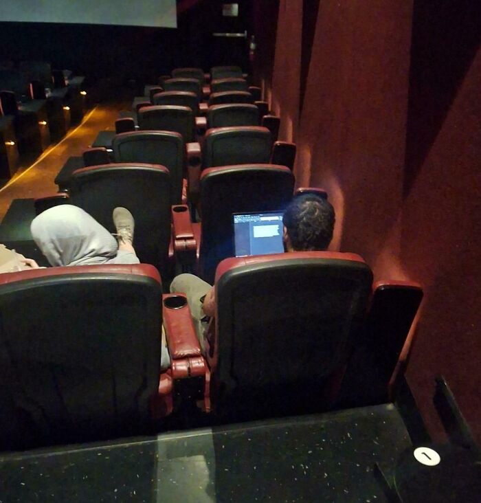Person using a laptop in a cinema, displaying inconsiderate behavior.