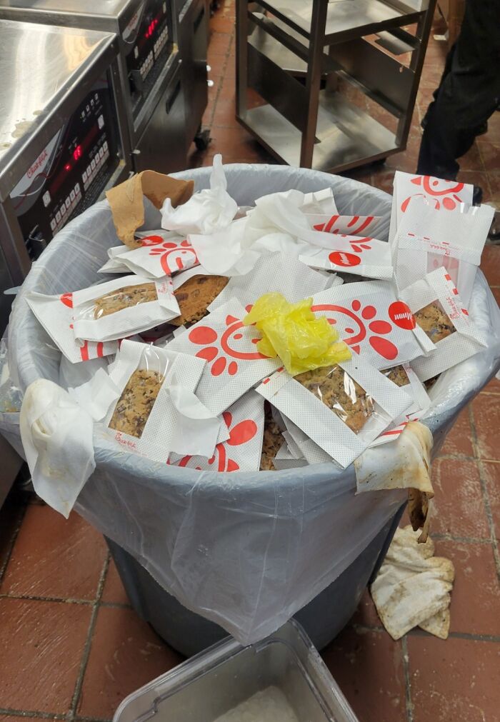 Trash bin filled with discarded packaged cookies, highlighting wasteful behavior typical of people being jerks.