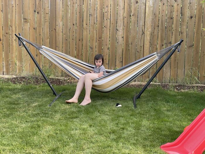 Child sitting in a hammock in a backyard, illustrating interesting not photoshopped photo moment.