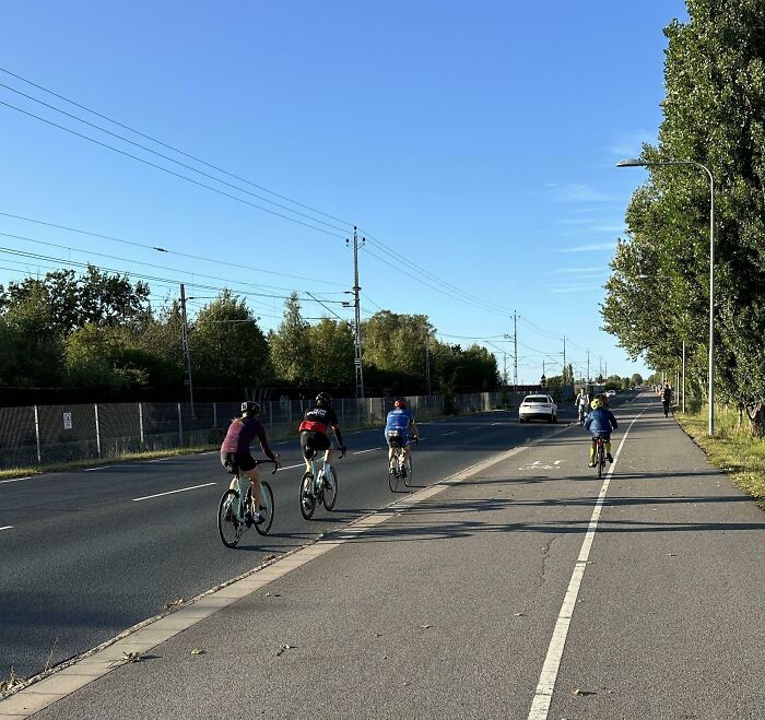 Cyclists riding on the road, blocking a car, exhibiting inconsiderate behavior.