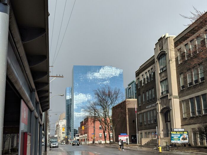 Glass building reflecting clouds, creating an interesting not photoshopped effect on an urban street.
