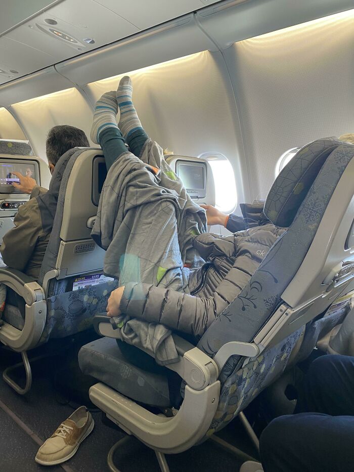 Passenger on a plane with feet up on the seat, displaying typical annoying behavior in a cramped cabin space.