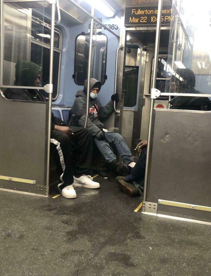 Public transport passengers sitting with feet stretched across in a train car.