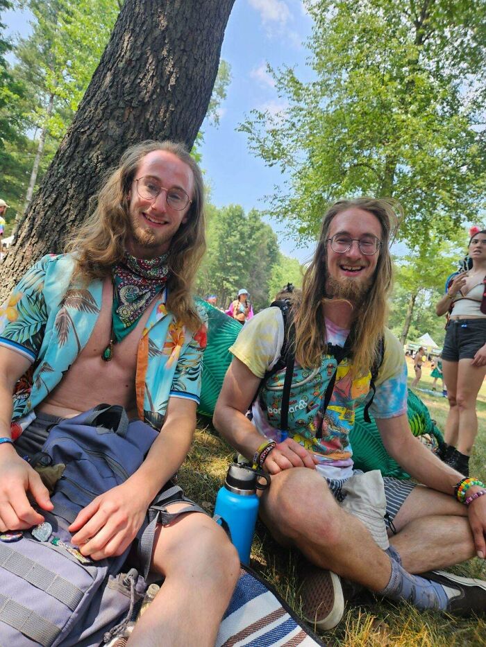 Two men resembling uncanny doppelgangers sitting outdoors with colorful attire and backpacks.