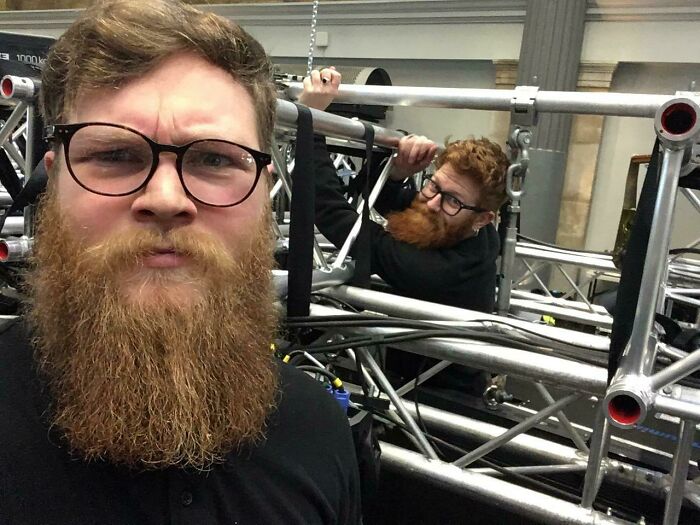 Bearded man in glasses stands near metal structure; uncanny doppelganger in the background creating a glitch effect.