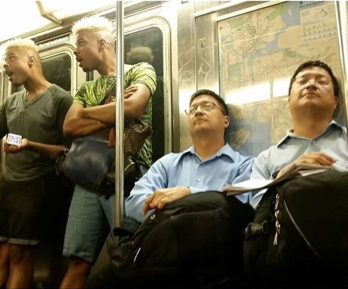 Uncanny doppelgangers on a subway, two pairs of lookalikes standing and sitting, depicting a glitch in the matrix.