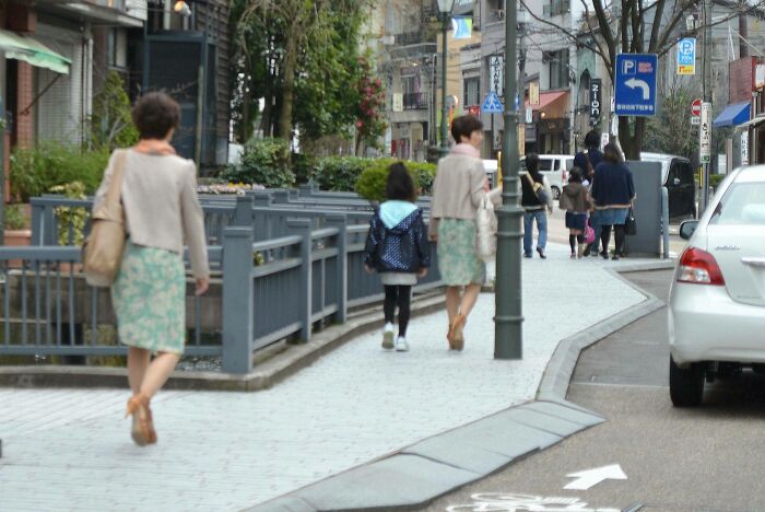Two women with similar outfits walk down a city street, creating an uncanny doppelganger effect.