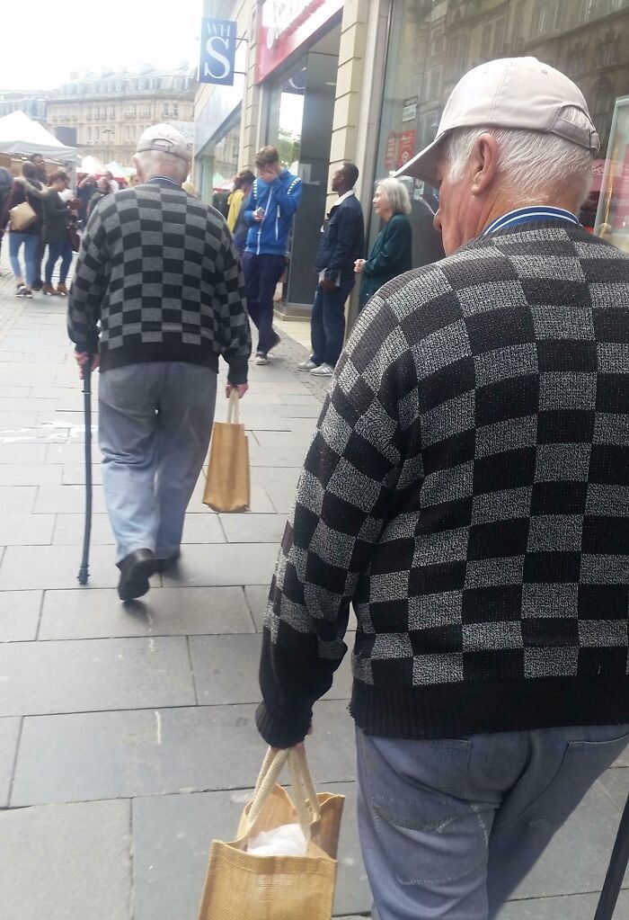 Elderly men in matching checkerboard sweaters walking, resembling uncanny doppelgangers.