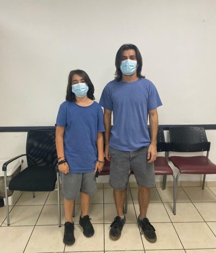 Two uncanny doppelgangers wearing blue shirts and masks, standing in a room with chairs.