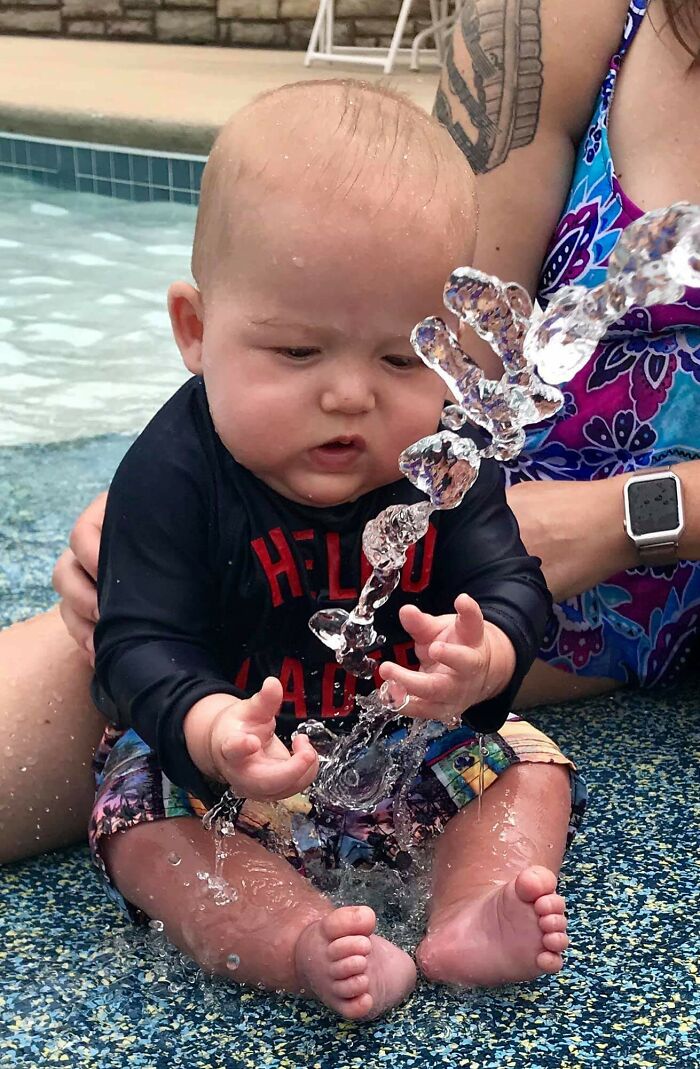 Baby playing with a splash of water, showing curious expression. Not photoshopped, capturing a candid summer moment at the pool.
