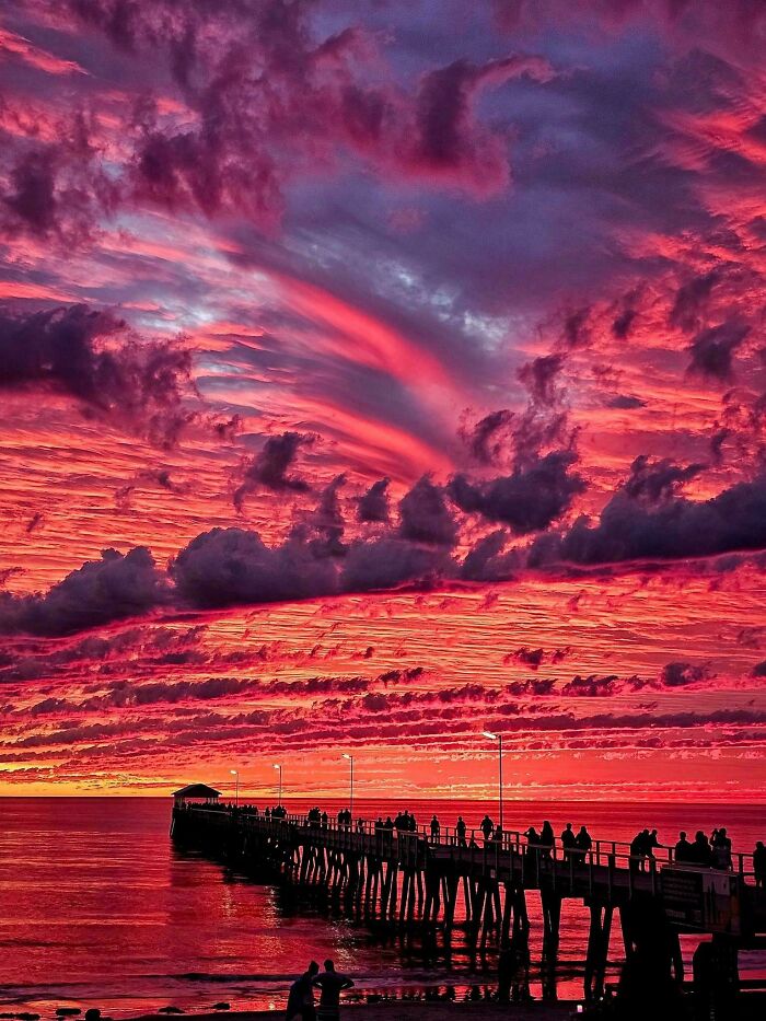 Dramatic sunset over a pier with vibrant pink clouds, capturing an interesting scene not photoshopped.