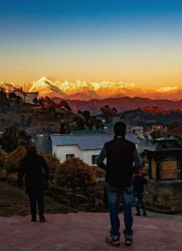 People admiring a stunning, not photoshopped sunset view of snow-capped mountains and a village.