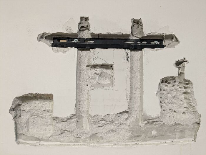 Wall with damaged drywall and an improperly installed bracket showing a clear DIY disaster mistake.
