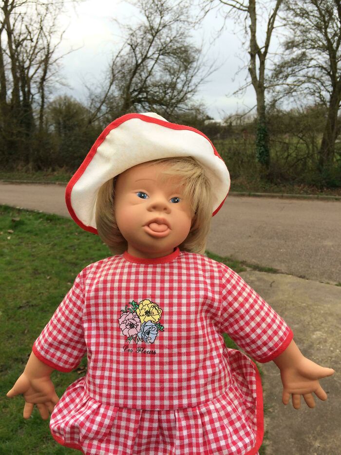 Doll with a playful expression in a red checkered dress and hat, showcasing creative designer flair outdoors.