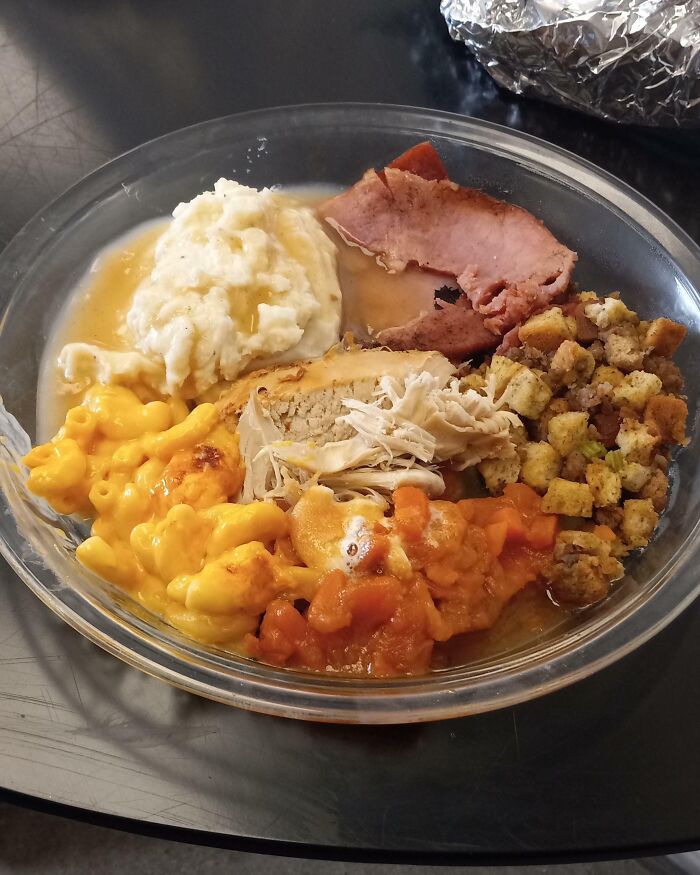 Thanksgiving meal with turkey, stuffing, mac and cheese, mashed potatoes, ham, and sweet potatoes on a glass plate.