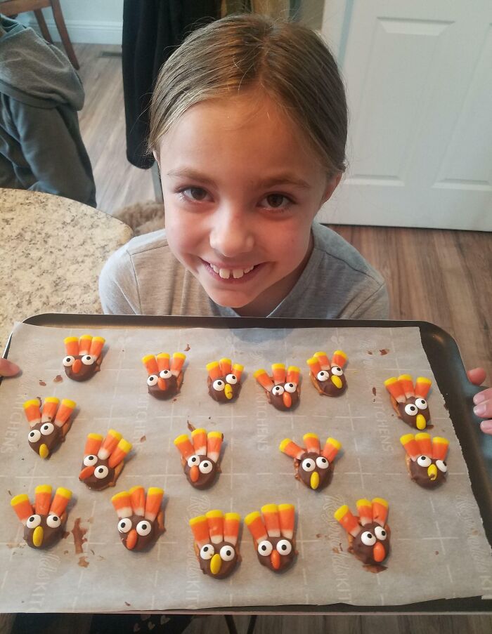 Smiling child holding a tray of Thanksgiving-themed chocolate treats shaped like turkeys.