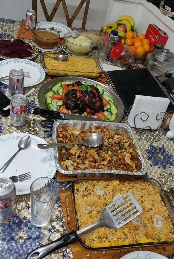 Thanksgiving feast on a table with roasted meat, casseroles, salad, mashed potatoes, gravy, and drinks.