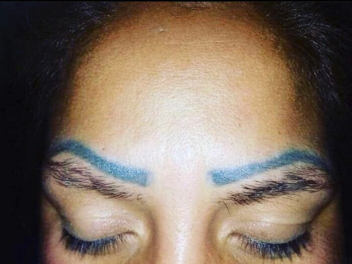 Woman with poorly done blue eyebrow tattoos, illustrating a tattoo mistake.