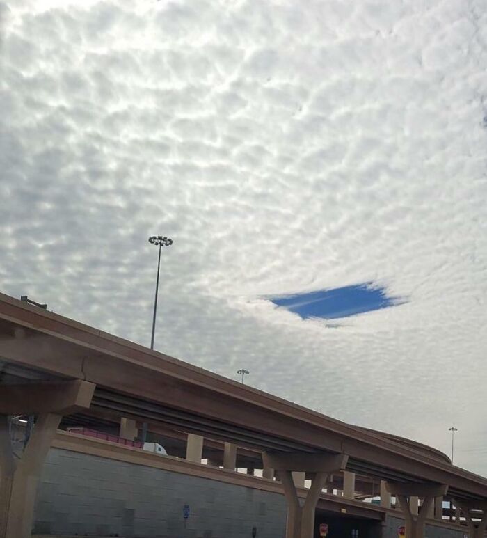 A cloud formation with a clear blue sky hole over a highway, showcasing an interesting not photoshopped photo.