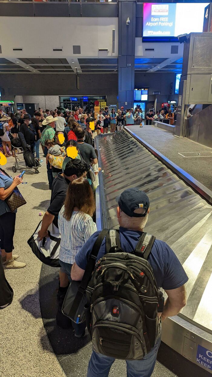 Crowded airport baggage claim with passengers waiting for luggage.