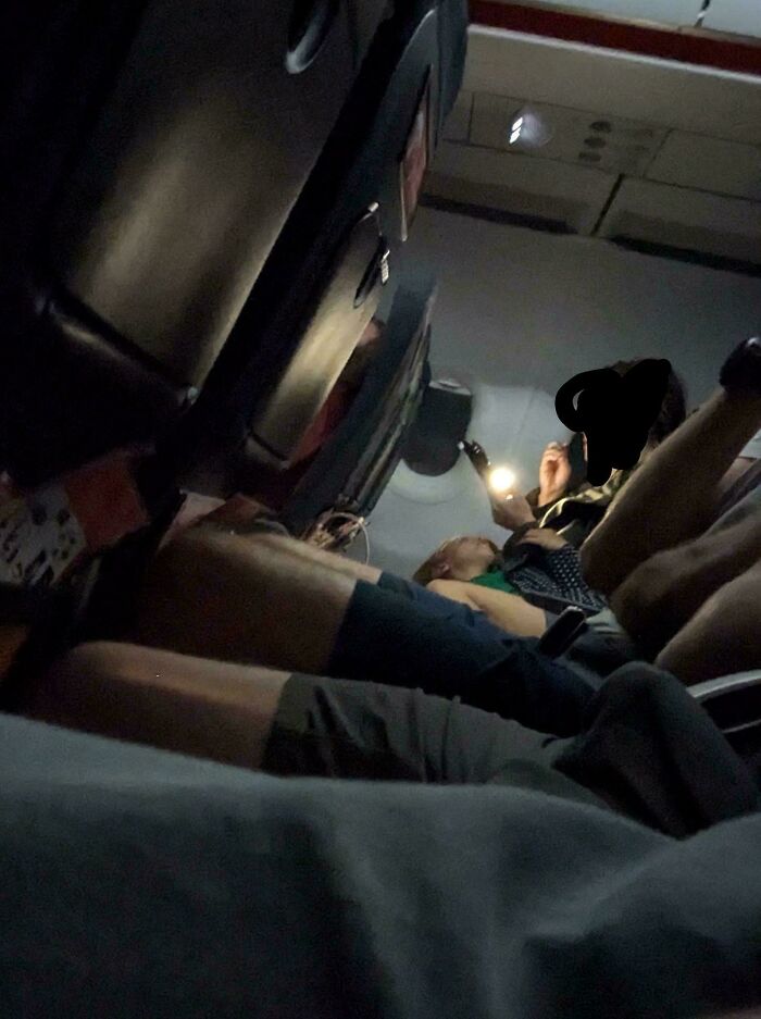 Passenger using phone flashlight on a plane, creating an annoying atmosphere for fellow travelers.