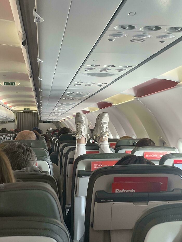 Passenger's feet in sneakers resting on plane seat, illustrating annoying plane behavior.