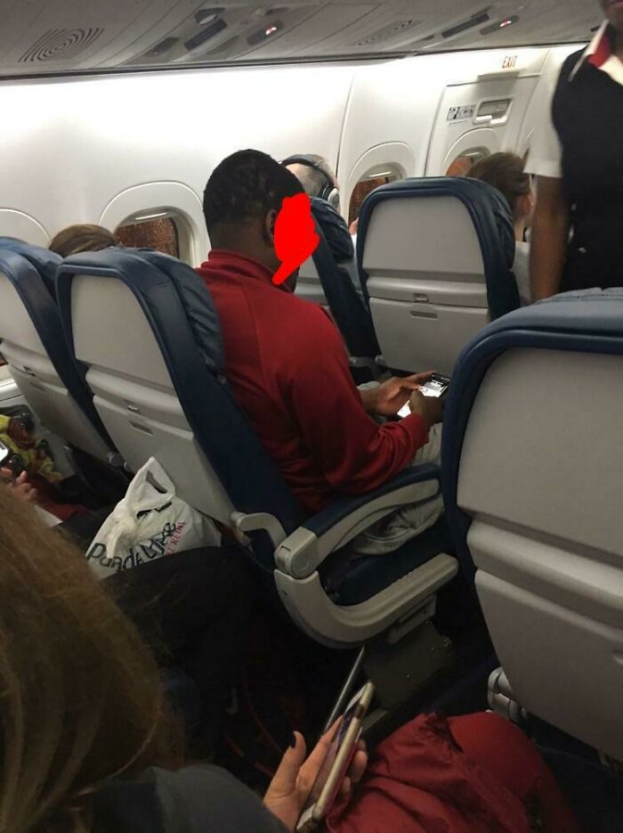 Passenger using phone with flash on in a dim airplane cabin, illustrating annoying plane passenger behavior.