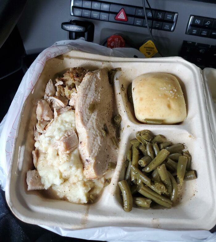 Thanksgiving meal with turkey, mashed potatoes, stuffing, green beans, and a roll in a disposable tray.