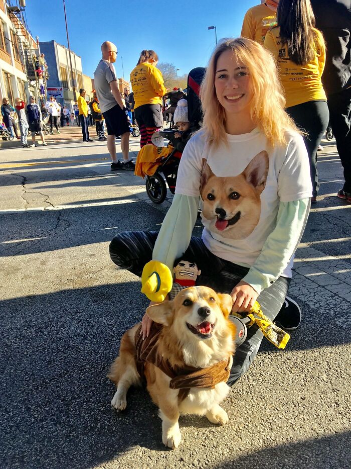 Woman in a Corgi shirt with her dog in costume at a festive outdoor event, embodying wholesome Thanksgiving vibes.