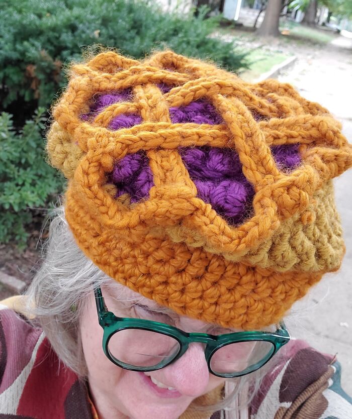 Person wearing a crochet hat designed like a pie with lattice top, showcasing a creative Thanksgiving look.