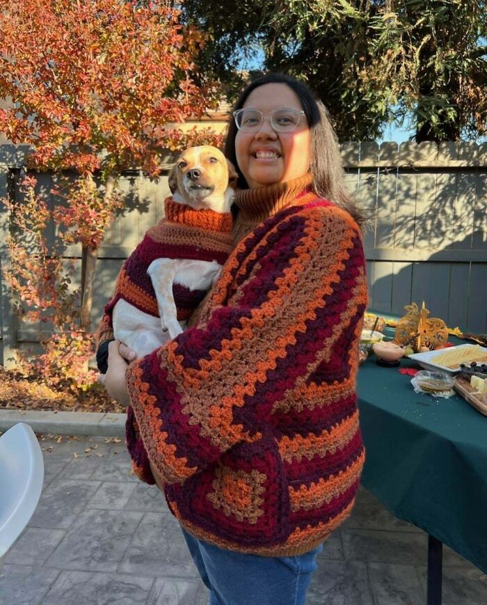 Person in a cozy, colorful sweater holding a matching dog, celebrating Thanksgiving outdoors.