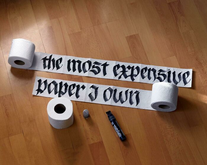 Creative handwriting on toilet paper, showcasing elaborate calligraphy text on a wooden floor.