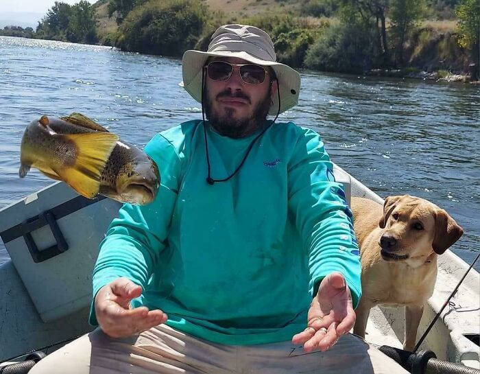 Man in a boat with a floating fish, wearing a hat and sunglasses, accompanied by a dog. Interesting, not photoshopped photo.