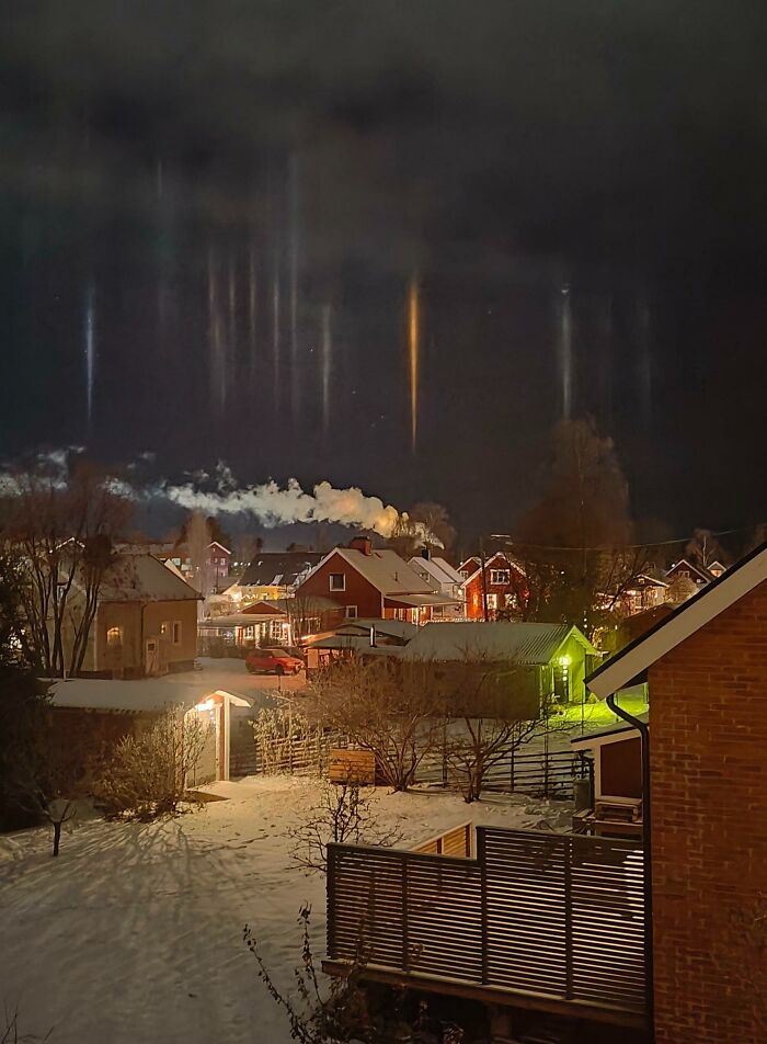 Snowy village at night with striking light pillars in the sky, showcasing an interesting not photoshopped phenomenon.