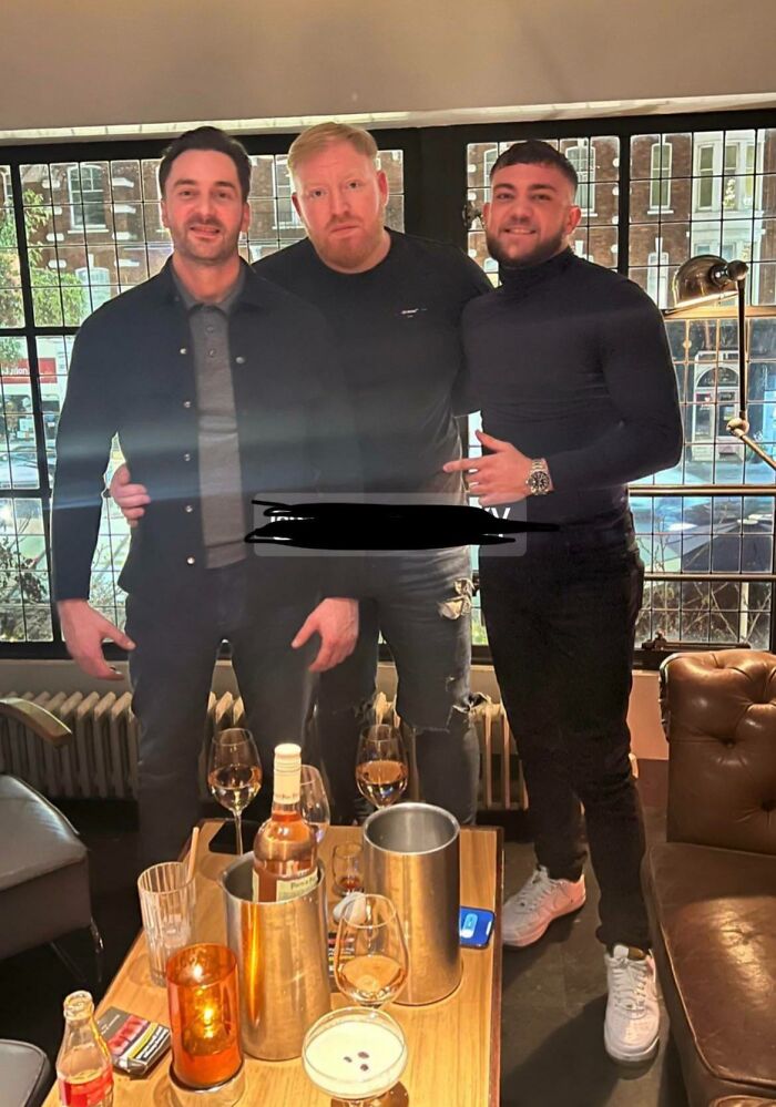 Three men standing together indoors, behind a table with drinks, in a non-photoshopped photo.