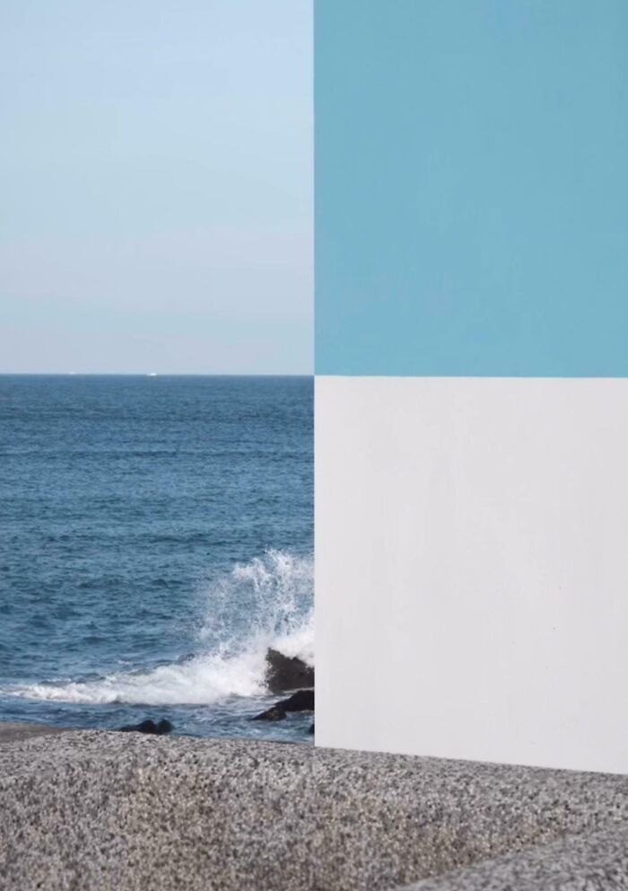 Ocean waves crashing against rocks, juxtaposed with a painted blue and white wall, showcasing interesting not photoshopped visuals.