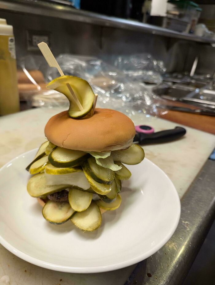 Burger overflowing with pickles on a plate, showcasing a food service worker's creative compliance with extra request.