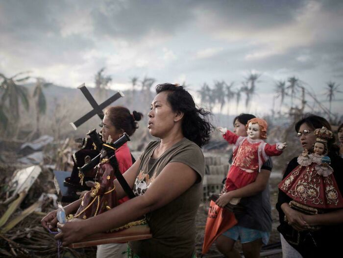 Women carrying religious statues, resembling a Renaissance painting amid a dramatic outdoor background.
